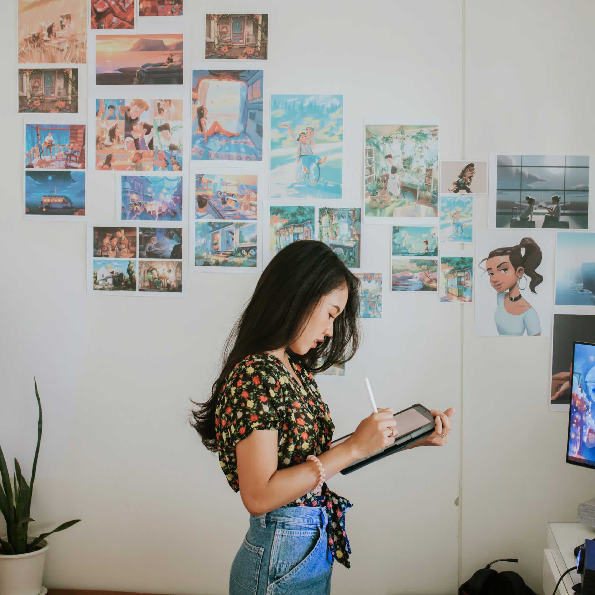 woman drawing on tablet wearing blue jeans and floral top