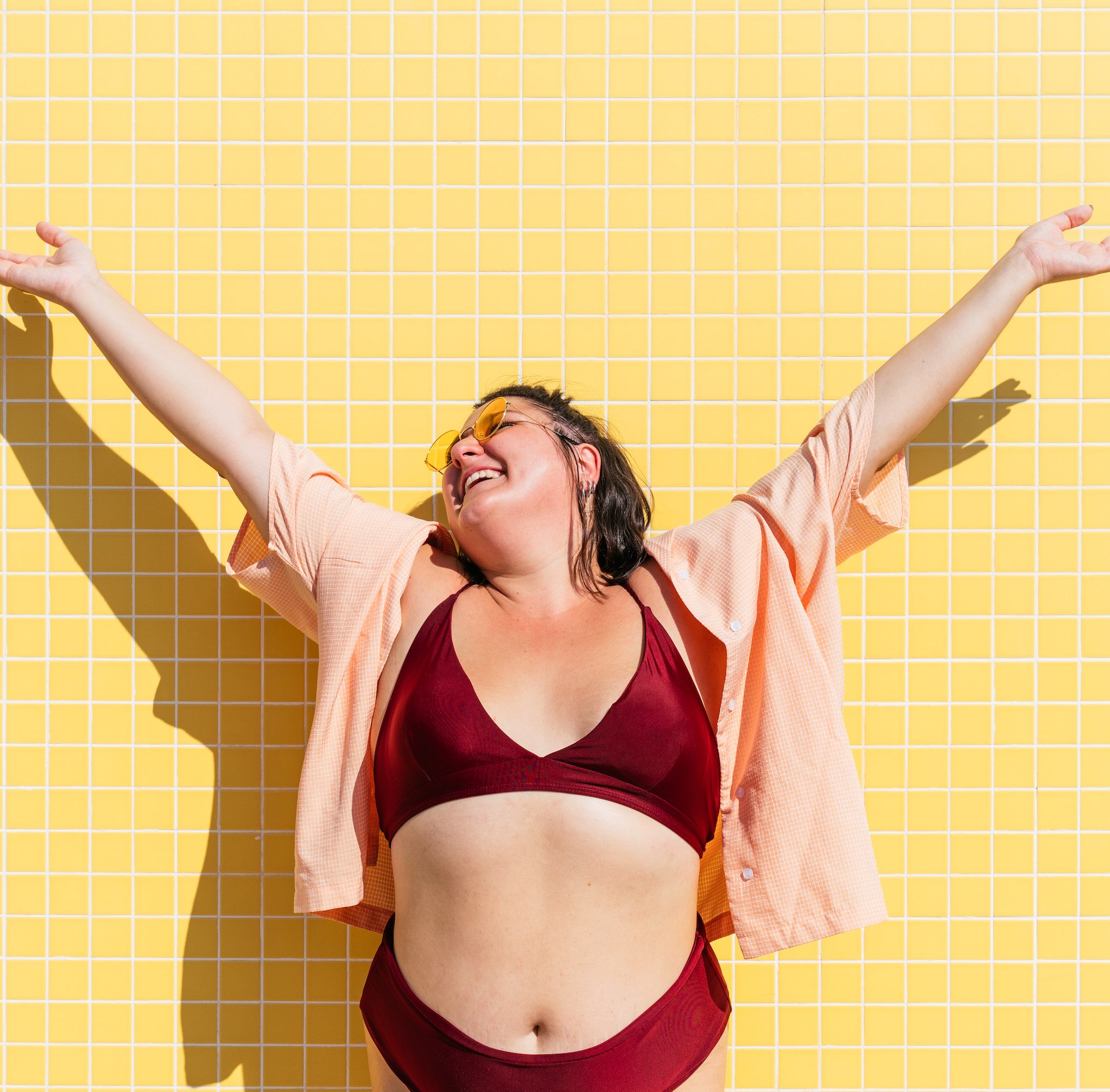 Beautiful and confident plus size woman having fun at the beach, posing on colorful wall background - concepts about body acceptance, body positive, self confidence and body care